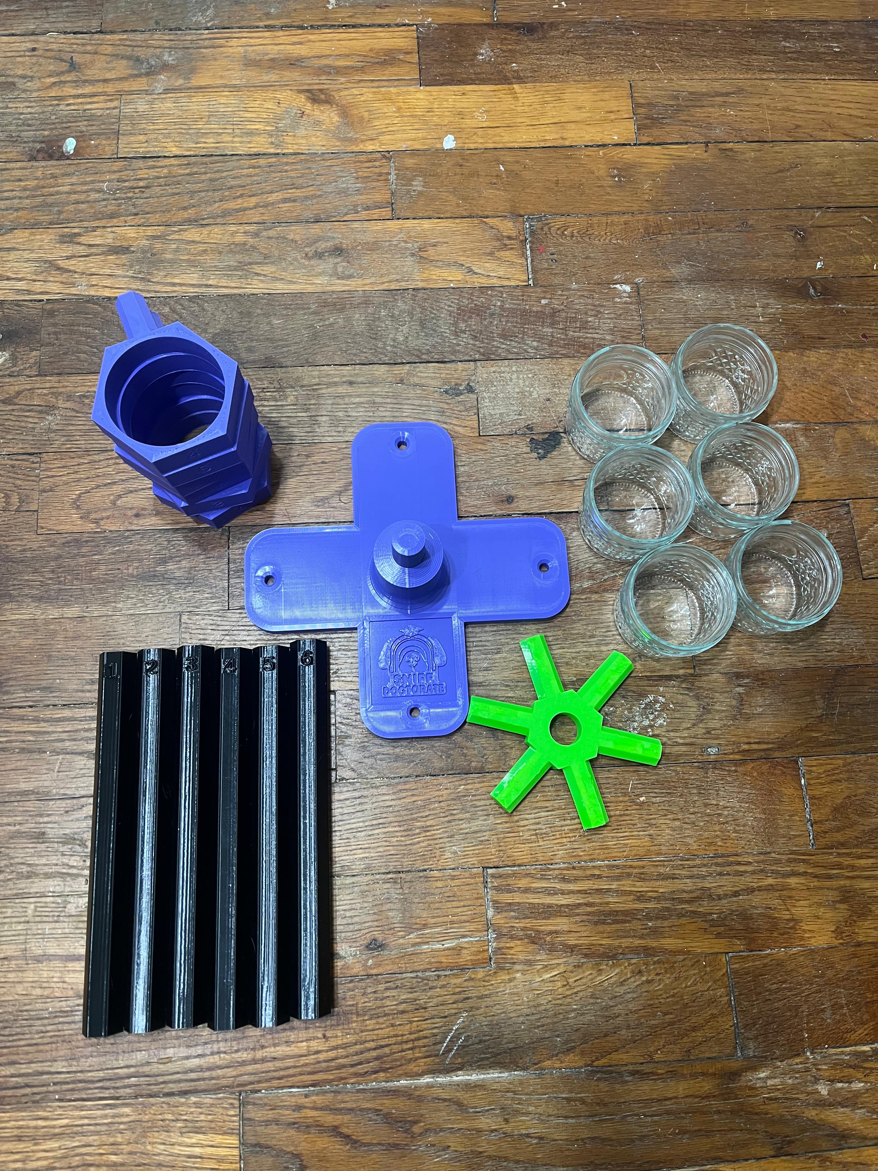 Photo shows the modular scent wheel taken apart; 6 glass ball jars, a plus sign shaped purple base with a place to put the spinner. The spinner is a lime green ring with 6 arm attachment spots sticking out. There are 6 black arms for the scent wheel, numbered 1-6. Finally, there are 6 purple glass cup holders with a similar attachment point to the lime green spinner. 