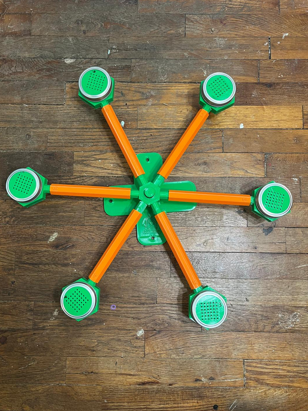 Scent wheel with a green base, green glass cup holders, green screens over the glass scent-holding jars, and orange  arms on a wooden floor