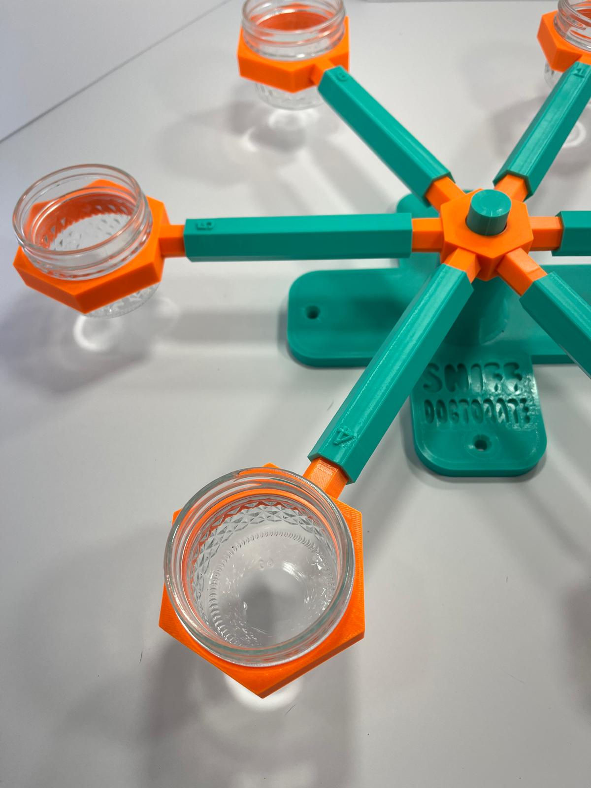 Scent wheel with bright orange scent cup holders and rotating spinners on a sturdy teal base and arms, built for professional detection dogs, AKC scent work trials, etc. scent cup holders have 4 oz glass jars for target odor. 